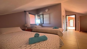 Una habitación de hotel con dos camas, una ventana con cortinas, una mesita de noche y una puerta que da a otra habitación.