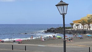 Une plage où des gens se prélassent au soleil et se baignent, un lampadaire et un bâtiment à la façade jaune.