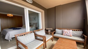 Une chambre d’hôtel moderne équipée d’un lit, de deux canapés, d’une table basse en bois et d’une grande porte-fenêtre coulissante donnant sur un balcon.
