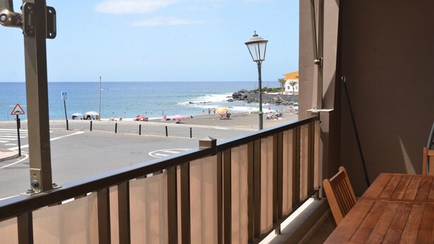 Un balcon donnant sur la plage, une rue avec un panneau indiquant un passage piéton et un lampadaire.
