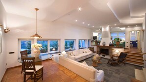 Amplia sala de estar con sofá, mesa de comedor y sillas, ventanas grandes y chimenea.