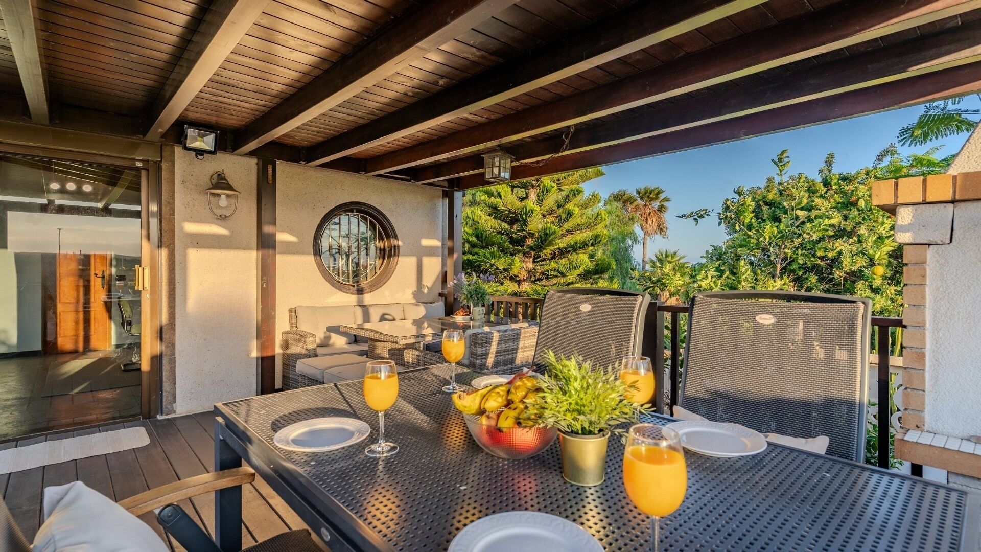 An outdoor dining area with a table set for two, a wicker chair, and a potted plant.