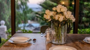 A dining table set with white plates, silverware, and a vase of white flowers.
