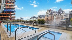 A rooftop pool with clear blue water, surrounded by a wooden deck and metal railings. In the background, there are historic buildings with distinctive architecture. - Waterfalls Hotel - Kings Corner - Resort Living (Victoria)