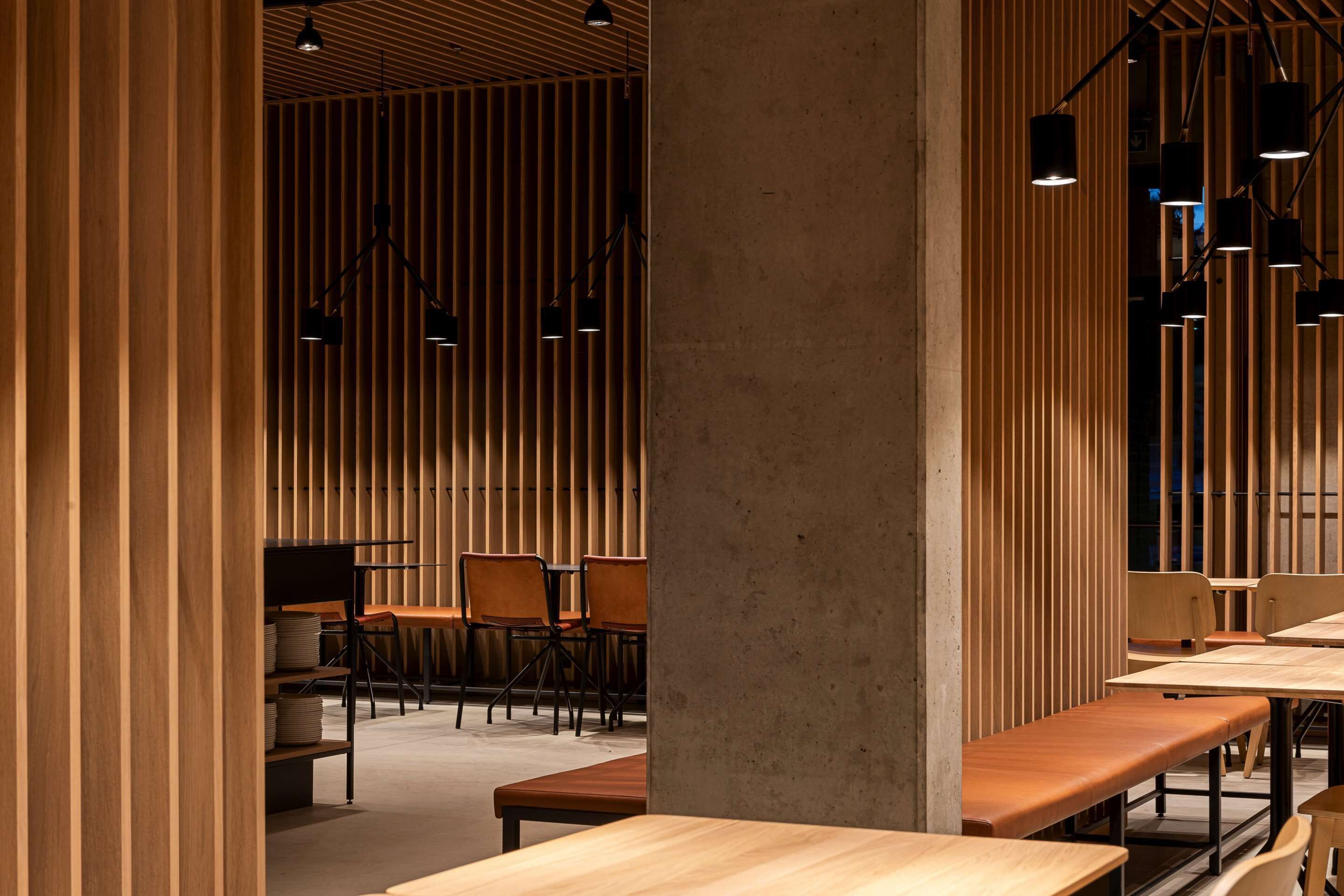 Un intérieur moderne avec des lambris en bois, des tables, des chaises et des luminaires suspendus.
