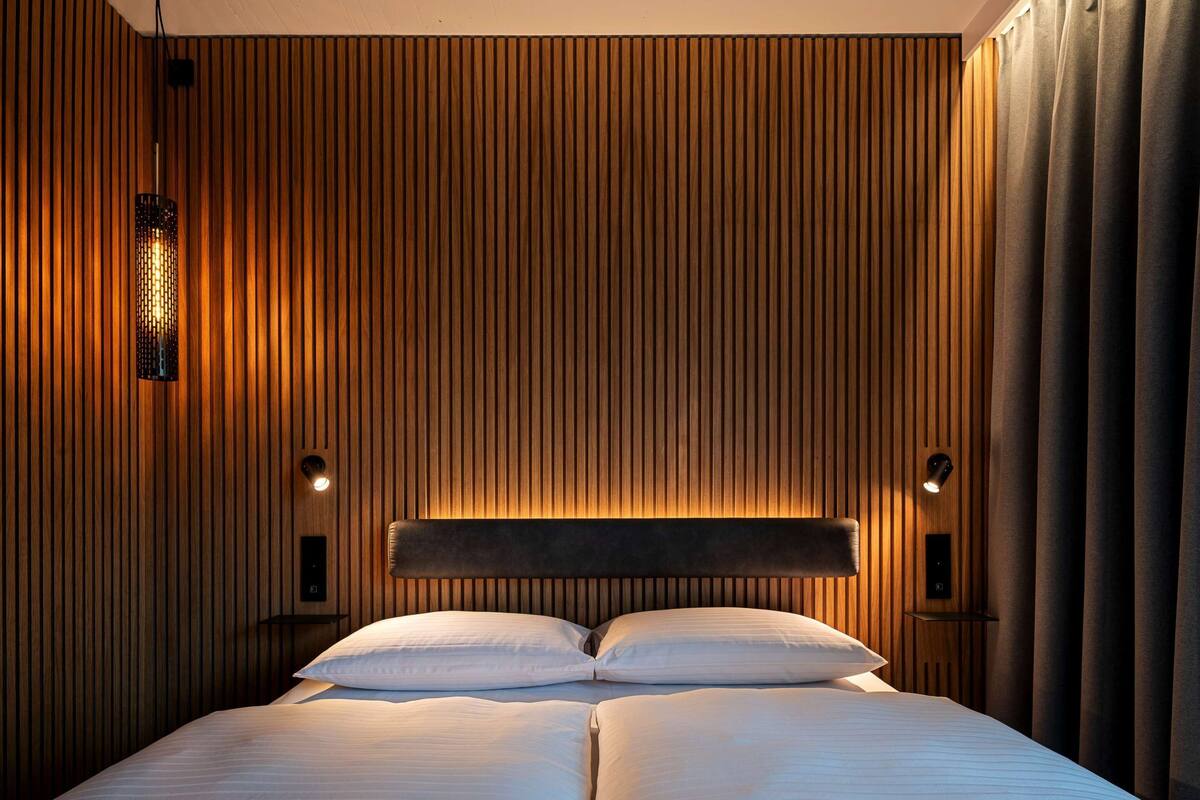 A modern hotel room with a large bed, wooden panel walls, and two bedside lamps.