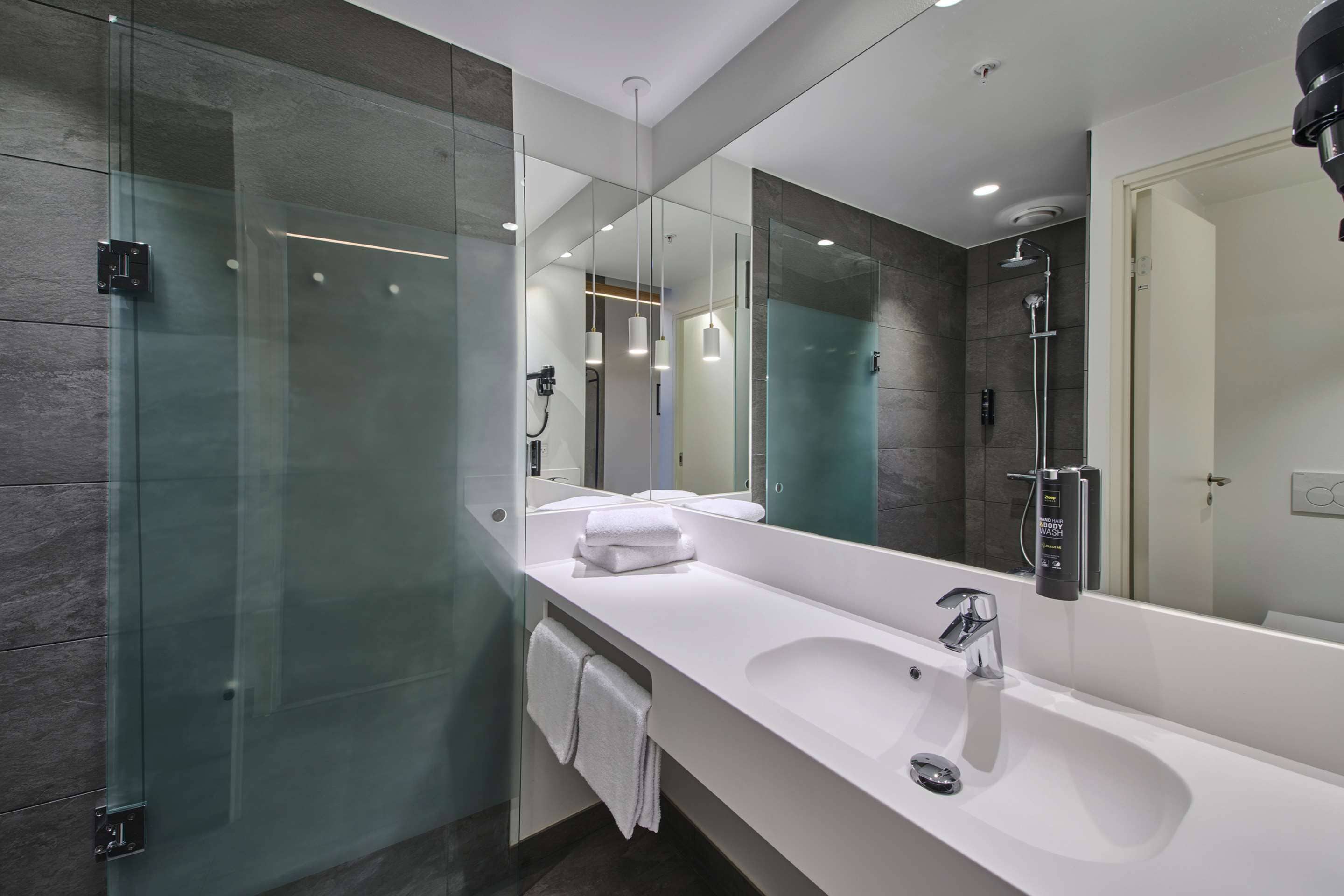 Un bagno moderno con un ampio specchio, un lavandino bianco e una cabina doccia in vetro.