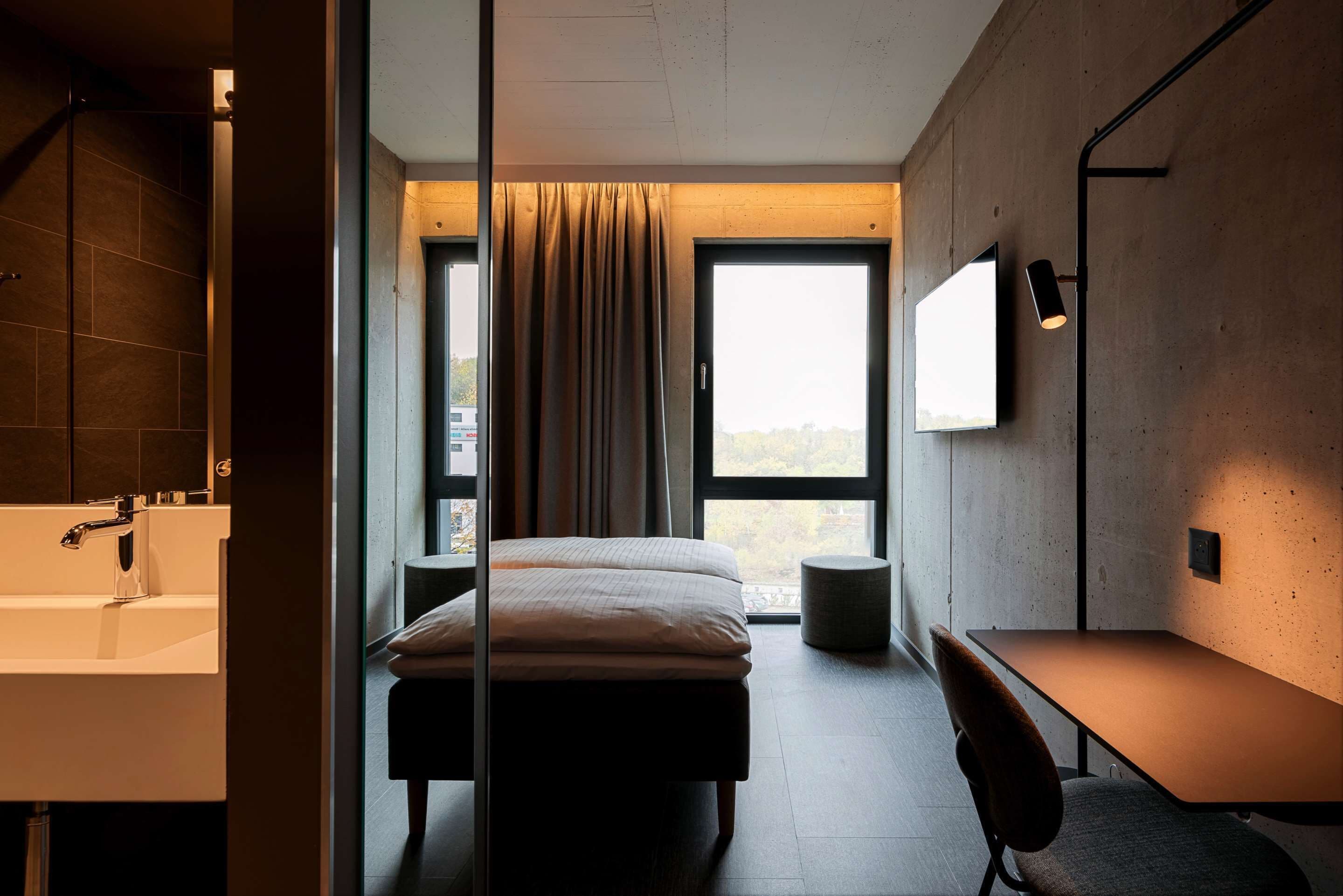 Un dormitorio moderno con una cama grande, un escritorio, una silla, un televisor y vistas al exterior a través de un ventanal.
