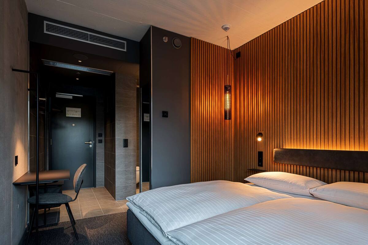 A modern hotel room with a bed, a desk, and a chair.