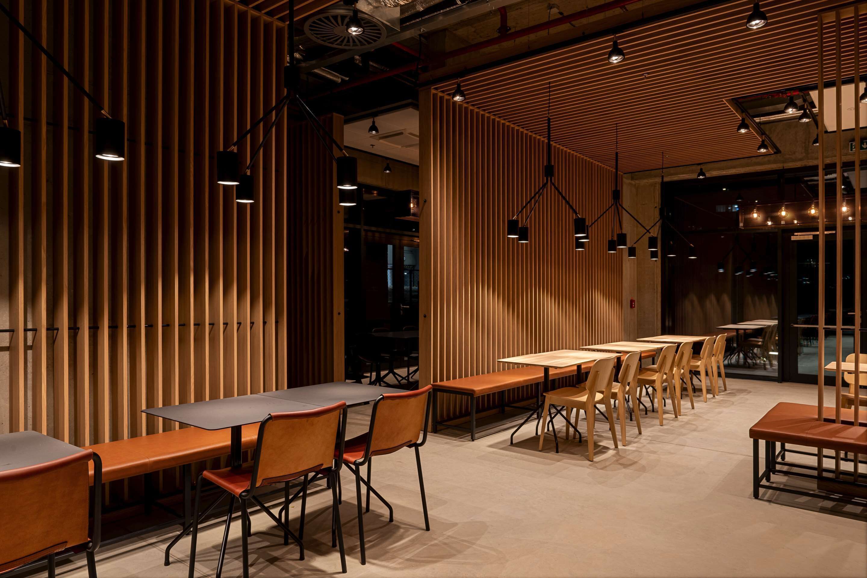 A modern restaurant interior with wooden panel walls, multiple dining tables, and chairs.