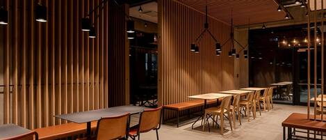 A modern restaurant interior with wooden panel walls, multiple dining tables, and chairs.