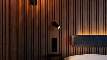 Ett modernt sovrum med en väggpanel av träribbor, ett sängbord med en lampa och en sänggavel.
