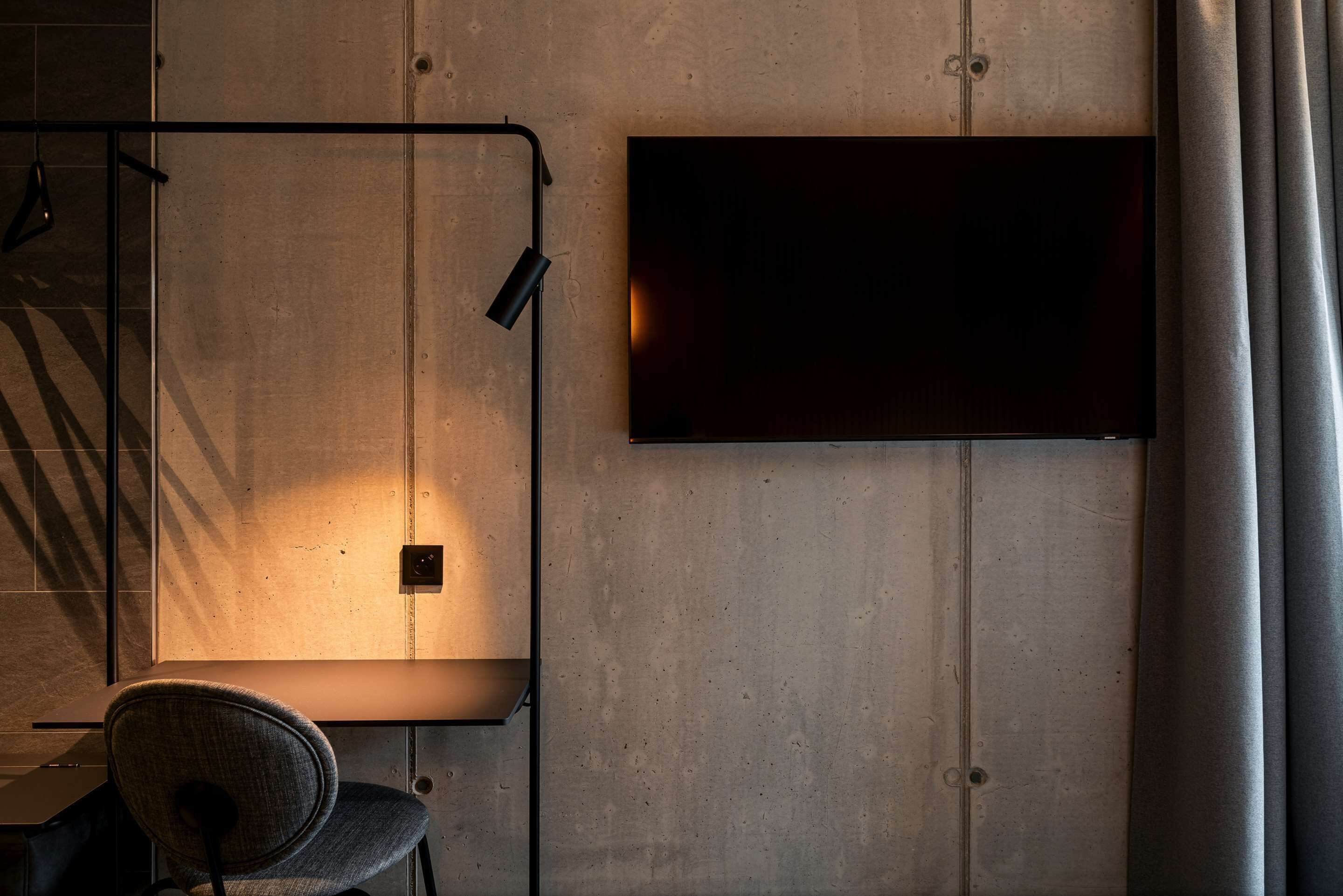 A modern room with a flat-screen TV mounted on the wall, a desk with a chair, and a lamp.