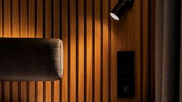 Una habitación de hotel moderna con un panel de madera en la pared, una cama con ropa blanca, un cabecero negro y una lámpara de pared.