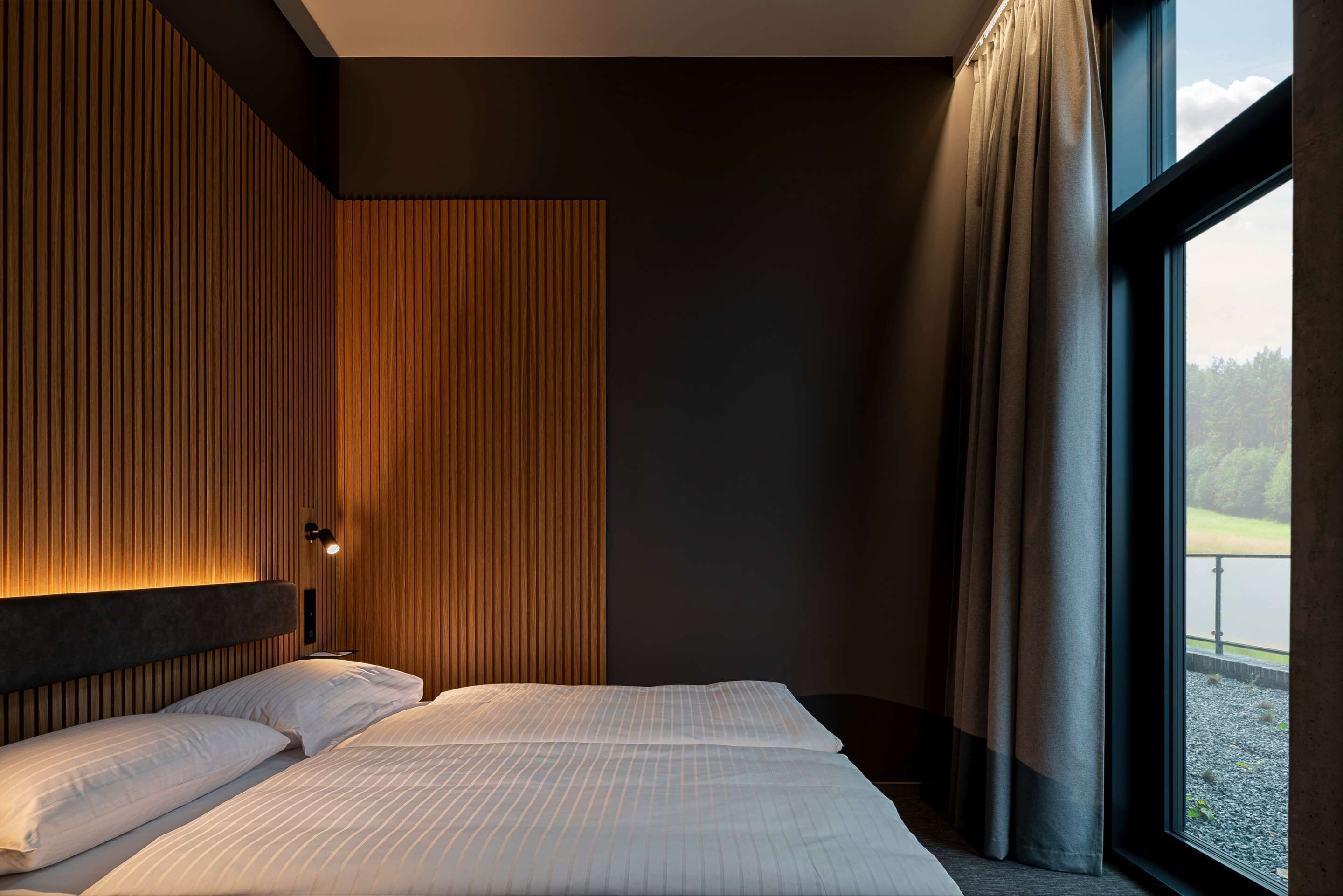 Ein modernes Hotelzimmer mit einem großen Bett, einer Wand aus Holzpaneelen und Blick auf einen See.