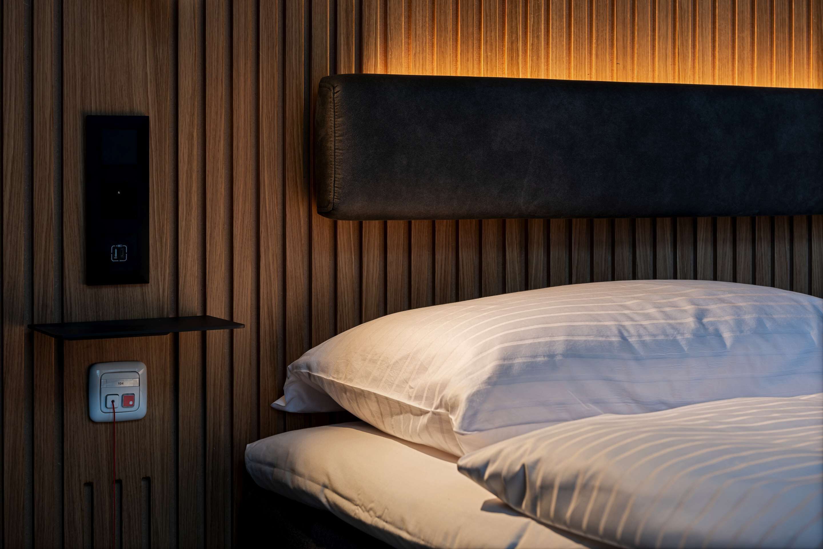 Une chambre à coucher avec une tête de lit en bois, une table de chevet dotée d’un panneau de commande et deux oreillers.