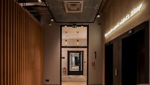 Een moderne hotel lobby met een houten lambrisering, een neonbord en een lift.