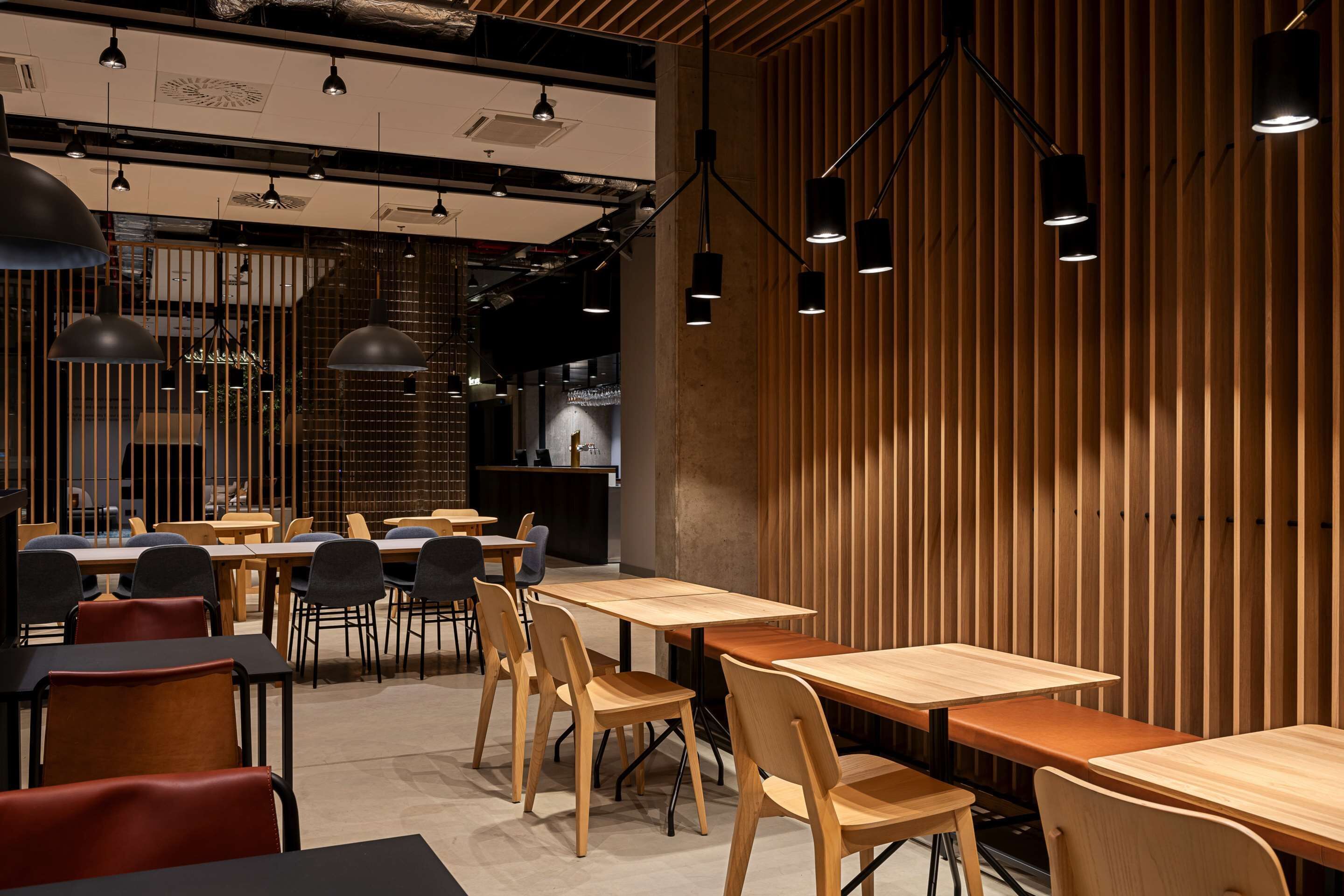 A modern restaurant interior with wooden tables and chairs, pendant lighting, and a wooden slat wall.