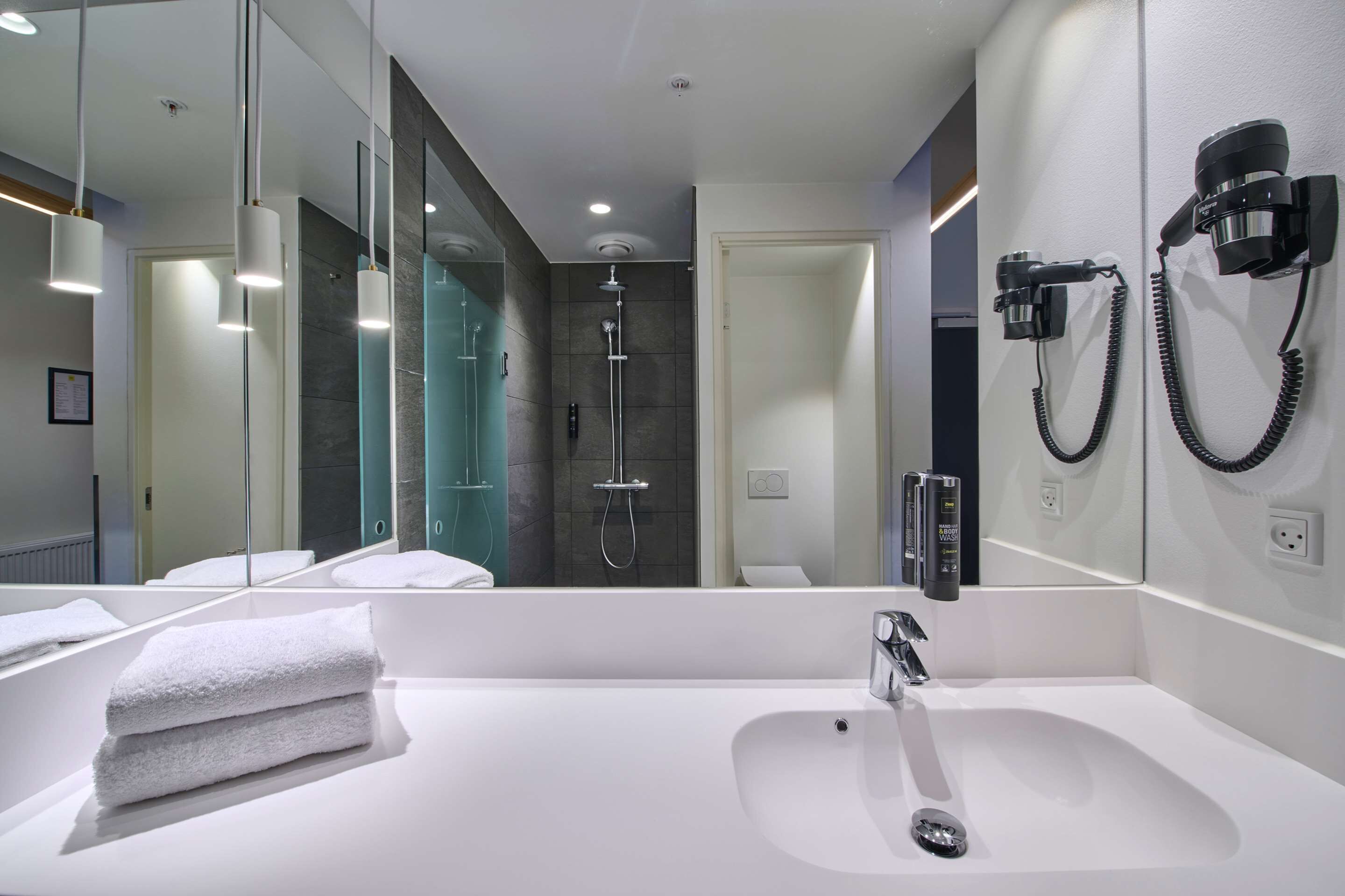 A modern bathroom with a large mirror, a white sink, and a shower area.