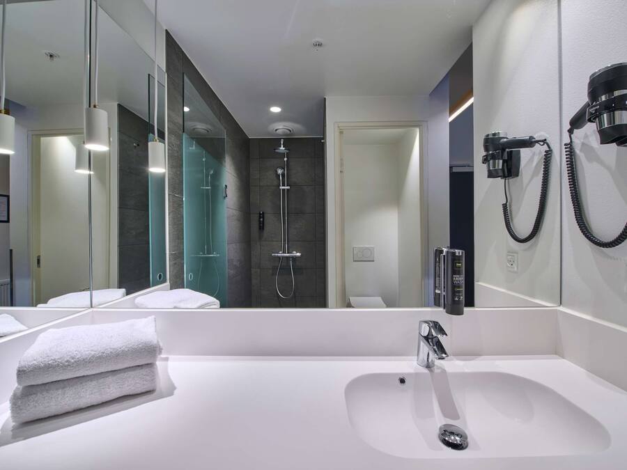 A modern bathroom with a large mirror, a white sink, and a shower area.
