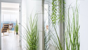 Un interior moderno con vistas al mar, un balcón con una silla y altas plantas de interior.