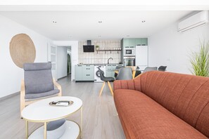 A modern living room with a sofa, a chair, a small table, and a kitchen in the background.