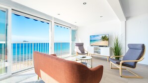 Un salón moderno con balcón vistas al mar, un televisor de pantalla plana y muebles contemporáneos.
