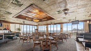 Un restaurante con techos altos, detalles de tallado intrincado, amplias ventanas con vistas al océano y una combinación de mobiliario de madera y metal.