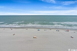A beach with people sunbathing and swimming, a clear sky, and calm ocean waves. - Ocean Front Views, Indoor and Outdoor Pools with Hot Tub, Pickleball & BBQs (Myrtle Beach)