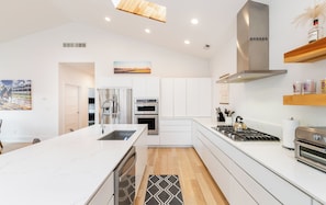Une cuisine moderne avec des meubles blancs, des appareils en acier inoxydable et un plancher en bois.