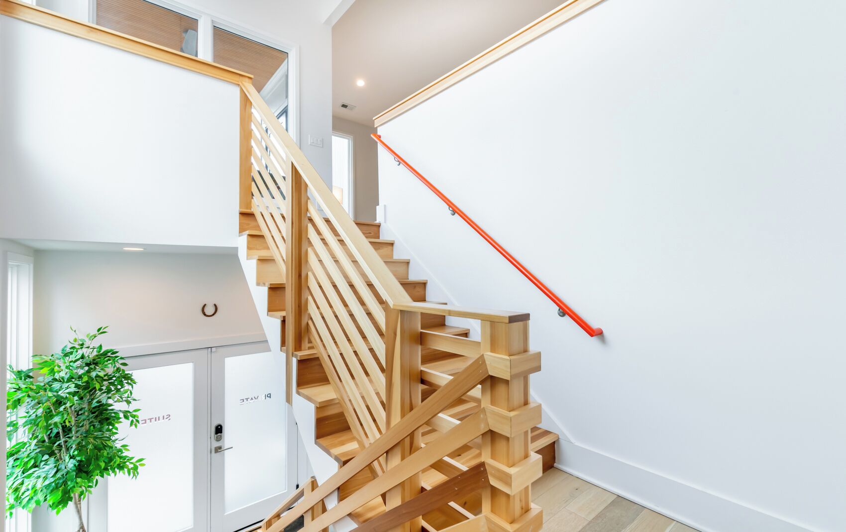 Een moderne trap met houten treden en een rode leuning, die naar een verdieping leidt.