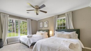 Une chambre d’hôtel avec deux lits, un ventilateur de plafond, de grandes fenêtres avec des rideaux et une vue sur la verdure.