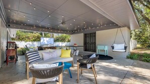 Un espace extérieur aménagé en terrasse, avec un mur en briques blanches, un fauteuil suspendu, un canapé avec des coussins et une table avec des chaises.