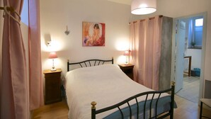 A bedroom with a bed, two bedside lamps, a painting on the wall, and a door leading to another room. - Gîte-appartement sur la Côte D'emeraude (Beaussais-sur-Mer)