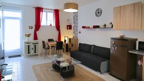 A modern living room with a glass coffee table, black sofa, wooden cabinets, and a red curtain. - Gîte-appartement sur la Côte D'emeraude (Beaussais-sur-Mer)