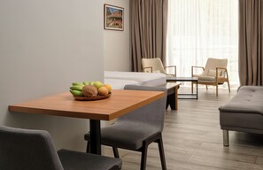 A hotel room with a wooden table, two gray chairs, a bed, and a window with curtains. - Voilà Beau Vallon (Mahé Island)