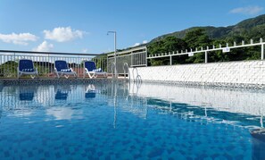 A swimming pool with clear blue water, surrounded by a white wall and a metal railing. There are lounge chairs along the poolside. - Voilà Beau Vallon (Mahé Island)