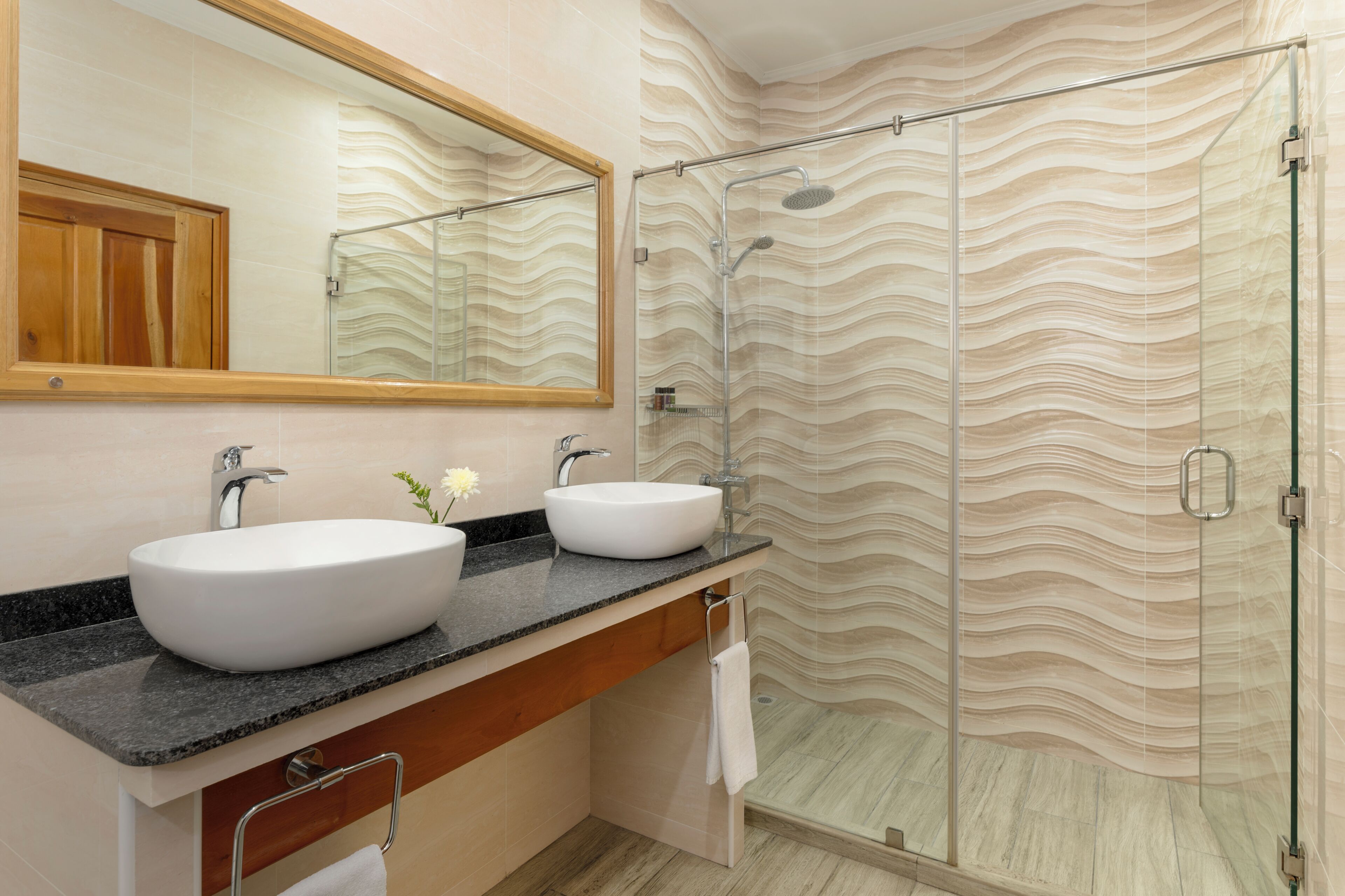 A bathroom with two sinks, a mirror, and a shower with a wavy wall design.