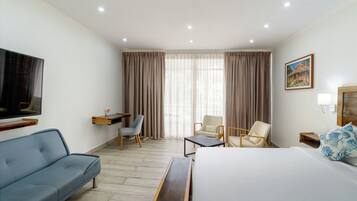A hotel room with a bed, a sofa, two chairs, a desk, a TV, and a painting on the wall.
