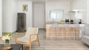 Eine moderne Küche mit einem Edelstahl-Kühlschrank, einer Holzeile mit Barhocker und einem Essbereich mit einer Couch und einem Sessel.