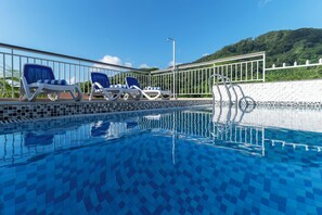 A swimming pool with blue tiles, two lounge chairs, a metal ladder, and a white fence. - Voilà Beau Vallon (Mahé Island)