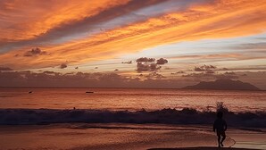 Eine Strandansicht mit Wellen, einem Sonnenuntergang und der Silhouette einer Person.