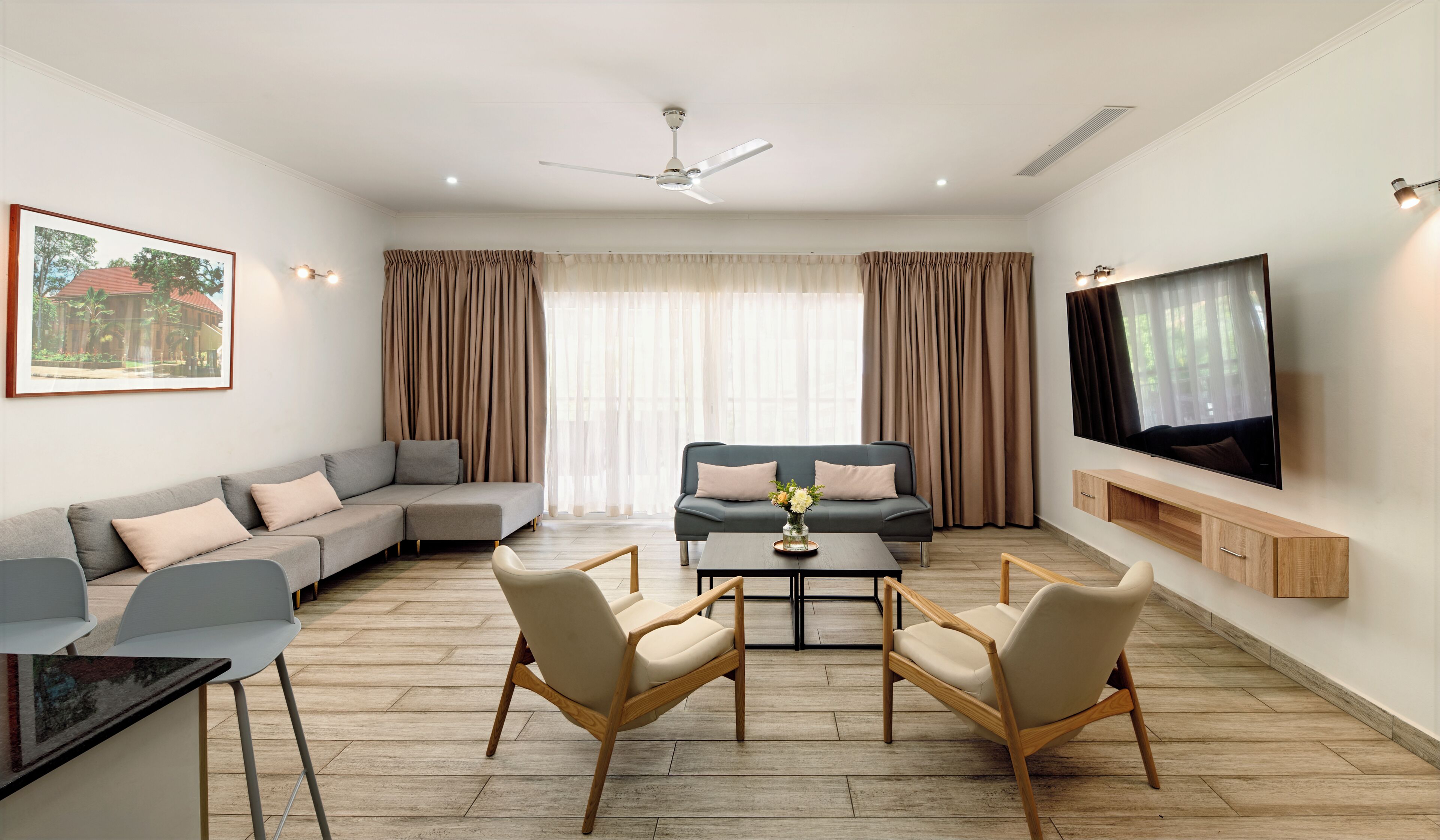 A modern living room with a sectional sofa, a smaller sofa, a coffee table, two chairs, a TV, and a ceiling fan.