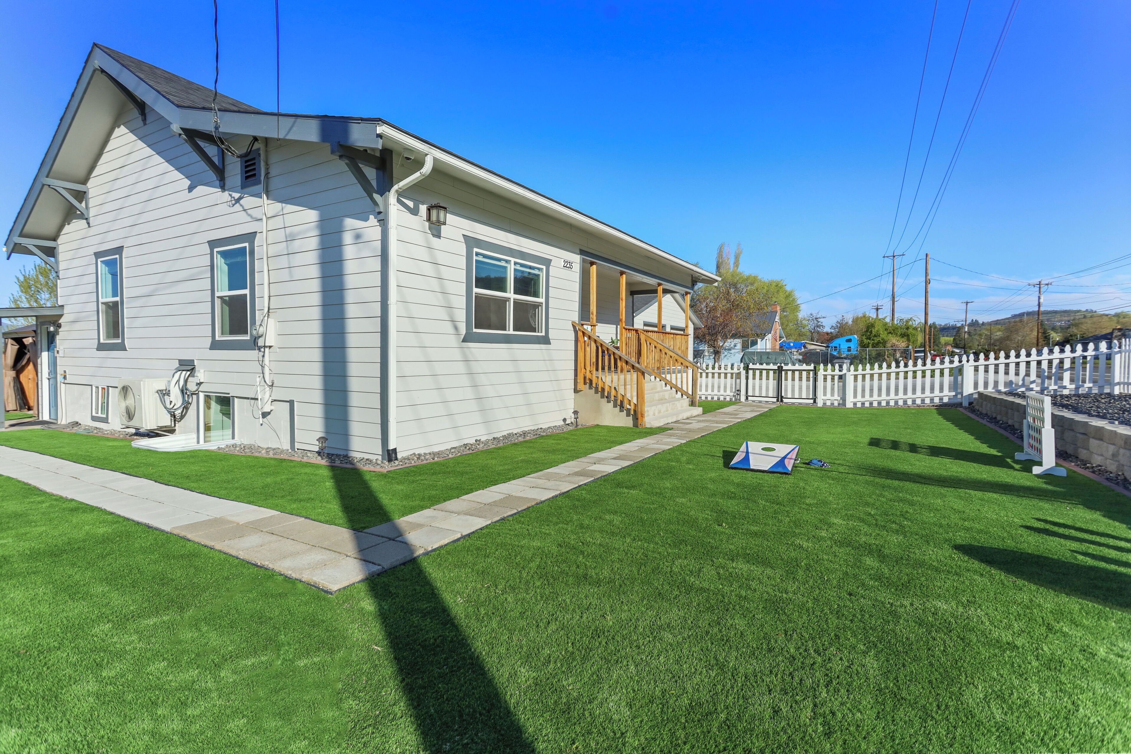 A single-story house with a front porch, a small front yard with a lawn, and a white picket fence.