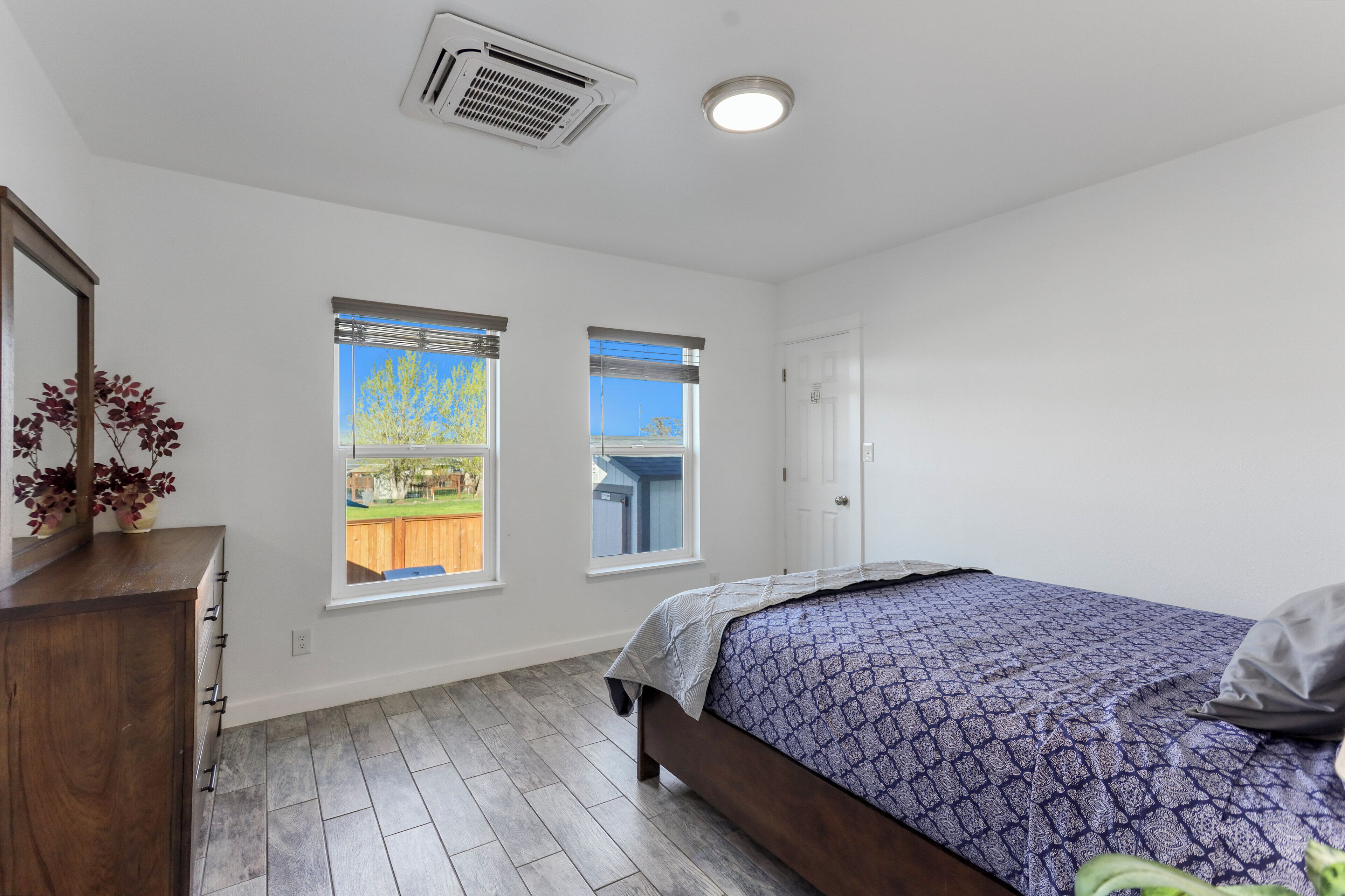 Une chambre à coucher avec un lit, deux fenêtres, une commode et une porte.