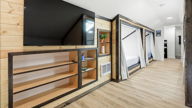 A modern hotel room with a flat-screen TV, wooden shelves, a potted plant, and a bed with curtains. - The Gather House! Super clean, Super comfortable and Super private! (The Dalles)