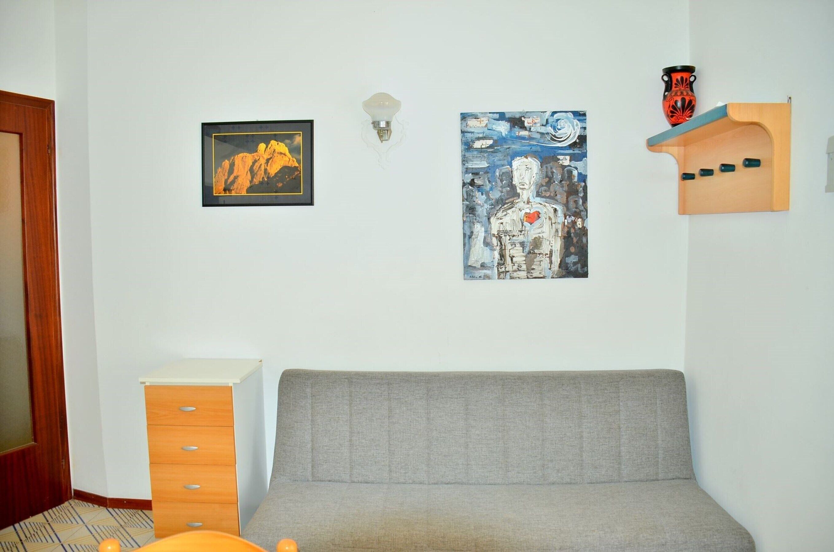 A room with a grey sofa, a wooden cabinet, and two artworks on the wall.