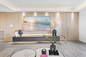 A modern living room with a large flat-screen TV, a minimalist console table, and a decorative plant.