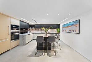 A modern kitchen with a marble island, two bar stools, and a large painting on the wall.
