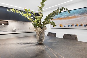 A modern kitchen with dark cabinets, a marble countertop, and a large vase with green foliage.